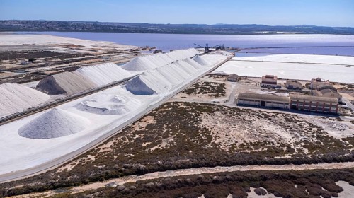 Aerial view of large salt cones forming alongside a pink lake and salt mine at sunset in