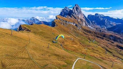 Paraglider over alpine meadows, in the background the peaks Sas Rigais and Furchetta of the Odle