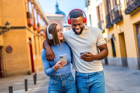 Multi-ethnic lovers embraced walking in the city using mobile phone and headphones