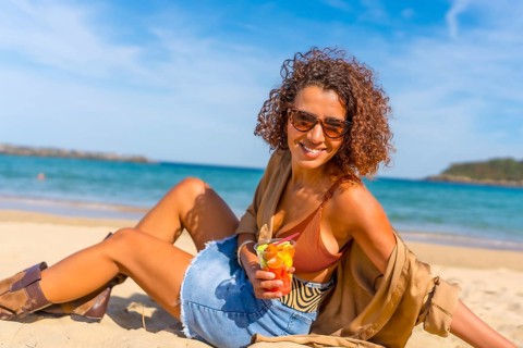 Happy sensual woman sitting on sandy beach enjoying tropical fruit sliced inside a plastic take