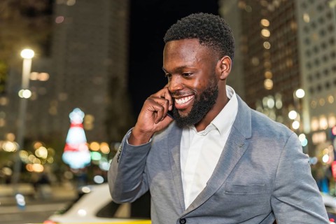 Young businessman smiling and chatting on a mobile phone while enjoying the vibrant city nightlife,