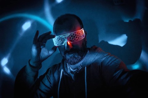 Bearded man adjusting futuristic glowing smart glasses in dark cyberpunk setting with blue and