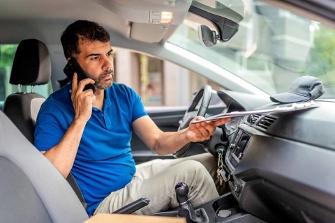 Mature caucasian male delivery person talking to the mobile phone sitting inside a van