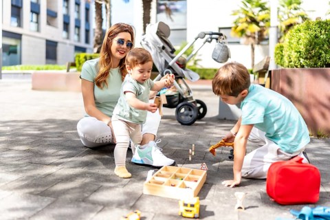 Full length photo of a happy woman and sons playing with toys in an urban space