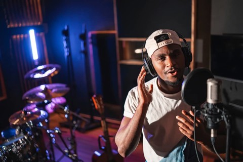 Young man recording vocals using a professional microphone and headphones in a music studio