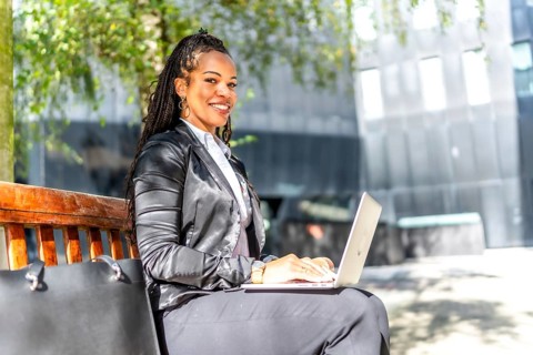 Side view portrait of a successful latin businesswoman working with laptop sitting on city bench