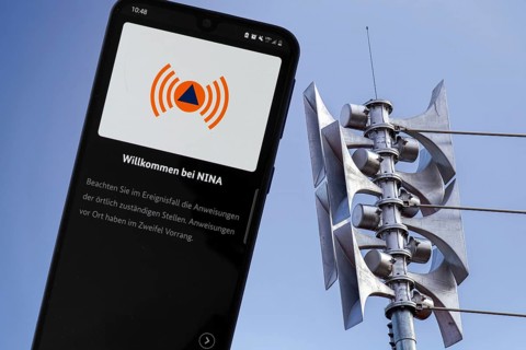 (Photomontage) Close-up of a siren at a school, next to it the open warning app NINA on a