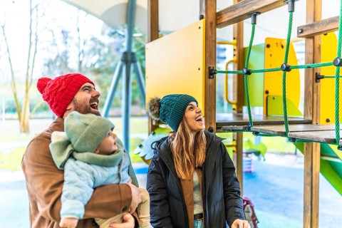 Cheerful parents and their baby are enjoying a playful day at the playground during wintertime