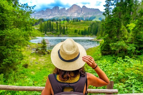Female tourist wearing straw hat enjoying the landscape of lake carezza with latemar mountain range