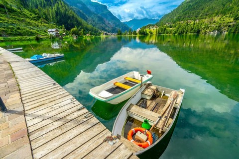 Wooden pier with boats reflecting in the emerald waters of alleghe lake with the dolomites in the