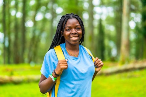 Portrait of a happy young african woman hiking through green forest