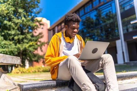 African man sitting at staircases on the university campus studying using laptop