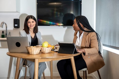 Two businesswomen are enjoying breakfast and working with laptop and tablet in their hotel room
