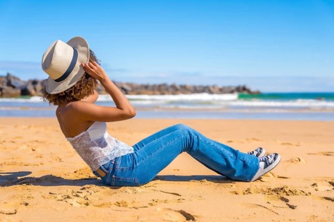 Side view of an unrecognzizable latin woman in summer denim clothes sitting on a beach gazing the