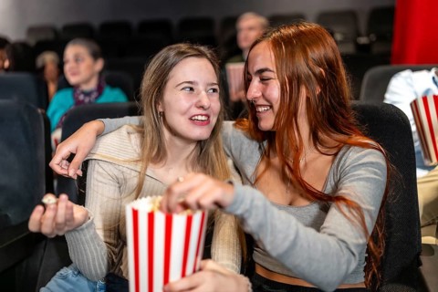 Two female friends enjoying a movie night, sharing popcorn and laughs, creating a joyful and