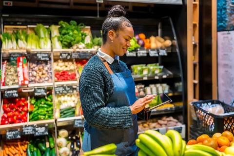 Smiling saleswoman wearing apron using digital tablet and managing inventory of fresh organic