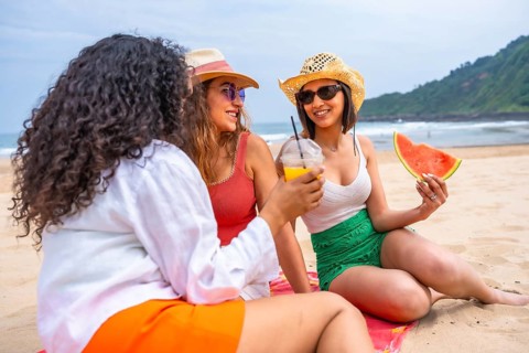 Multiethnic female friends enjoying summer on the beach on vacation, outdoors talking sitting on