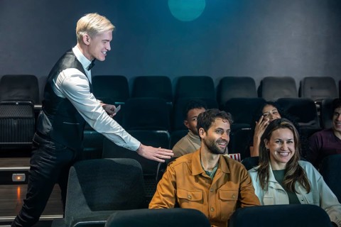 Movie theater usher guiding spectators to their seats and checking tickets, ensuring a smooth movie