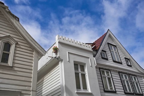 View upwards to white wooden houses with striking architecture under a clear blue sky, Bergen,