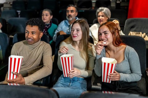 Group of friends watching a film at the movie theatre, eating popcorn and enjoying their leisure
