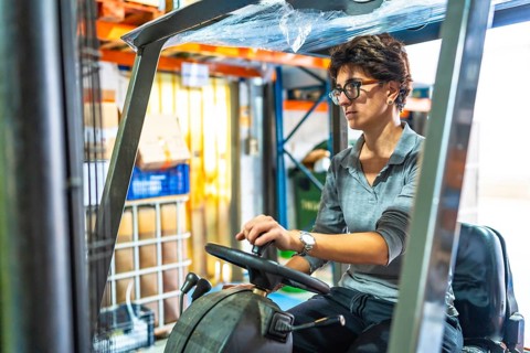 Caucasian adult woman driving a forklift in a warehouse