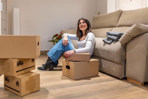 Young woman taking a break from unpacking, sitting on the floor of her new apartment and looking up