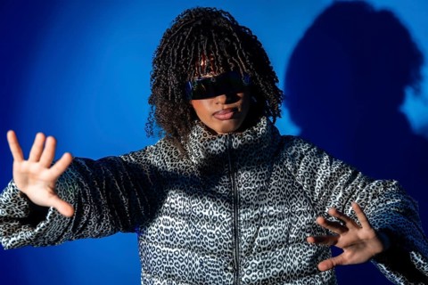Fashionable woman with curly hair wearing futuristic sunglasses and animal print jacket making stop