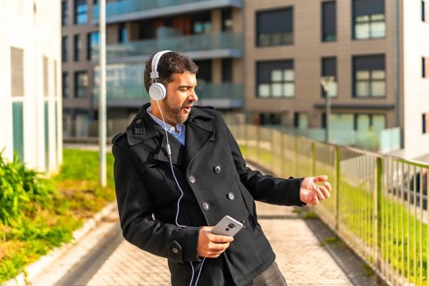 Adult caucasian businessman in casual winter clothes dancing while listening to music with mobile