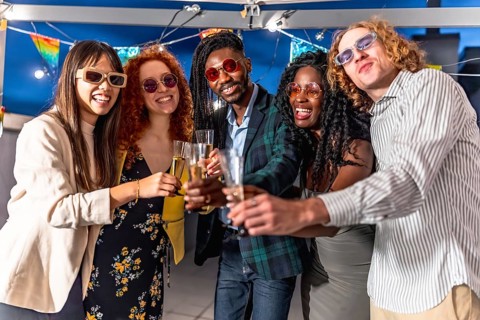 Elegant multiracial friends toasting with champagne together looking at camera at night party in a