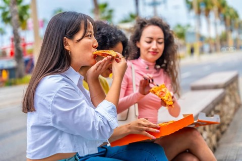 Multi-ethnic women sitting in the city enjoying a take away pizza together