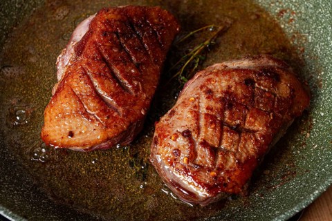 Cooking duck breast, in a frying pan, fried, with spices and herbs, close-up, no people