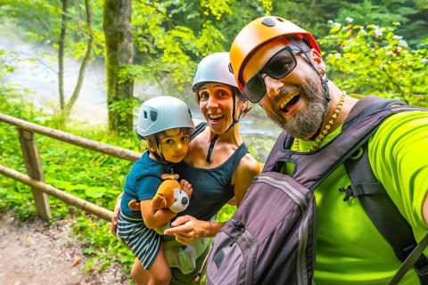 Happy family wearing helmets taking a selfie while hiking on a trail next to a river in vintgar