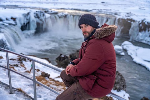 Portrait of a man hiker at frozen Godafoss waterfall at sunset in winter, Iceland, Europe