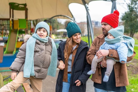 Happy family enjoying a delightful winter day at the playground, bundled up in warm clothes,