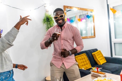 African man with pink t-shirt and sunglasses smiling drinking beer and dancing enjoying a home