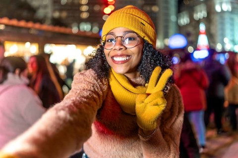 Smiling young woman wearing yellow winter clothes taking a selfie at a christmas market showing