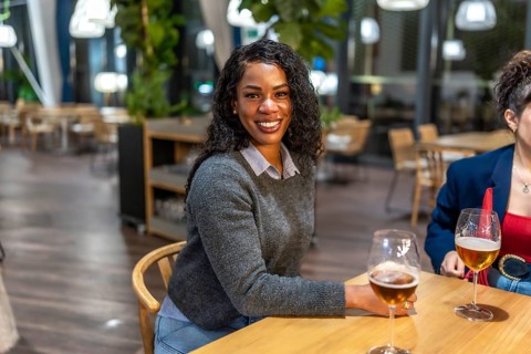 Latin woman smiling at camera sitting on a bar terrace with friends enjoying fresh beer