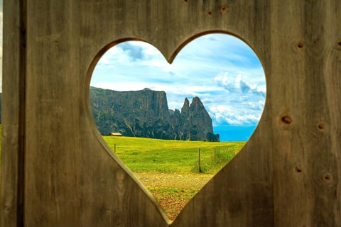 Breathtaking view of the italian dolomites, seen through a heart shaped opening in a wooden fence,