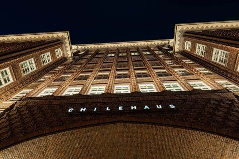 Symmetrical inner courtyard of a Kontorhaus at night, rows of windows and brick façade illuminated,
