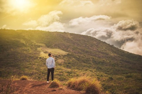 Rear view of a lonely man on top of a hill looking at the horizon. Back view of lonely man on a