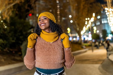 Smiling tourist wearing winter clothes looking up at christmas lights in a city center at night