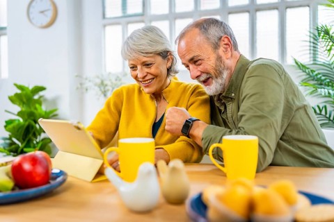Happy married senior couple using tablet together while sharing breakfast at home