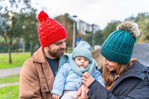 Smiling parents holding their baby wearing warm winter clothes and enjoying a winter day outdoors