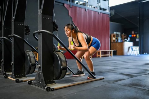 Full length photo of an asian strong woman pulling down weights using lat machine in a gym