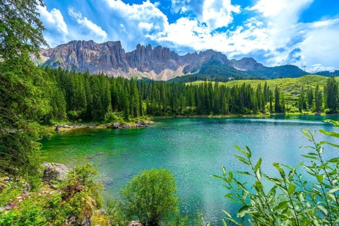 Emerald waters of lake carezza reflecting latemar mountain range in the dolomites, italy, on a