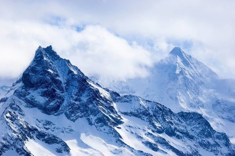 Wisps of mist surround the snow-covered peaks of the mountains Le Besso and Obergabelhorn, Val