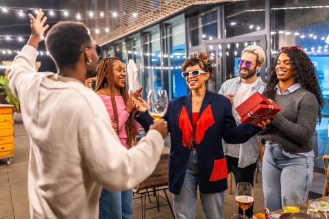 Multiracial friends celebrating surprise birthday party for a woman at night in the terrace of a