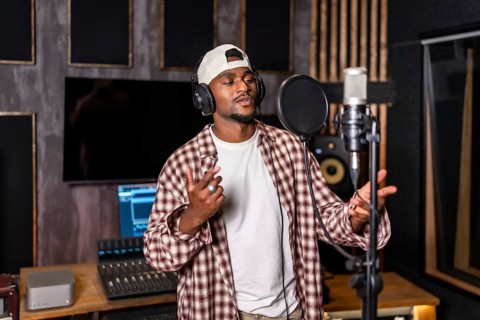 Young artist wearing headphones and singing into microphone while recording a song in professional