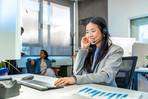 Young asian manager wearing headset working with computer in a coworking office, colleagues talking