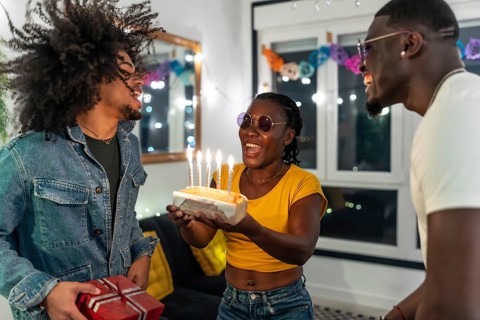 Young multiracial people surprising a friend with birthday cake and gift during night party at home